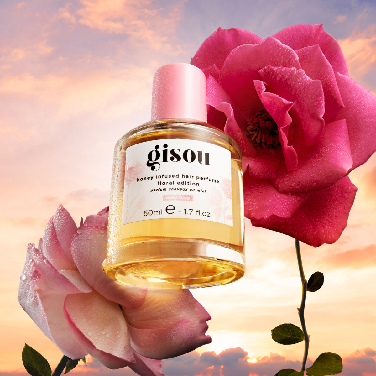 Gisou Honey Infused Hair Perfume Wild Rose 50ml bottle with pink roses against a soft sky background.