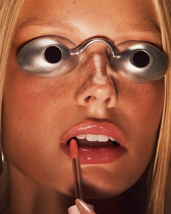 Model applying lip oil with goggles on.