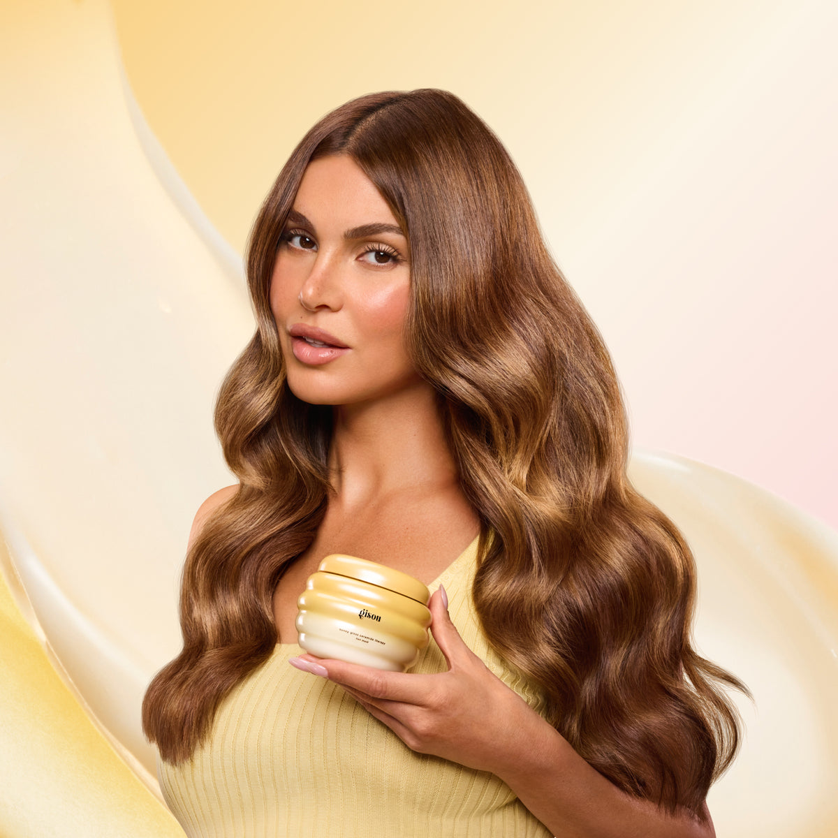 Negin Mirsalehi holding honey gloss ceramide therapy hair mask jar, showcasing long smooth and glossy waves.
