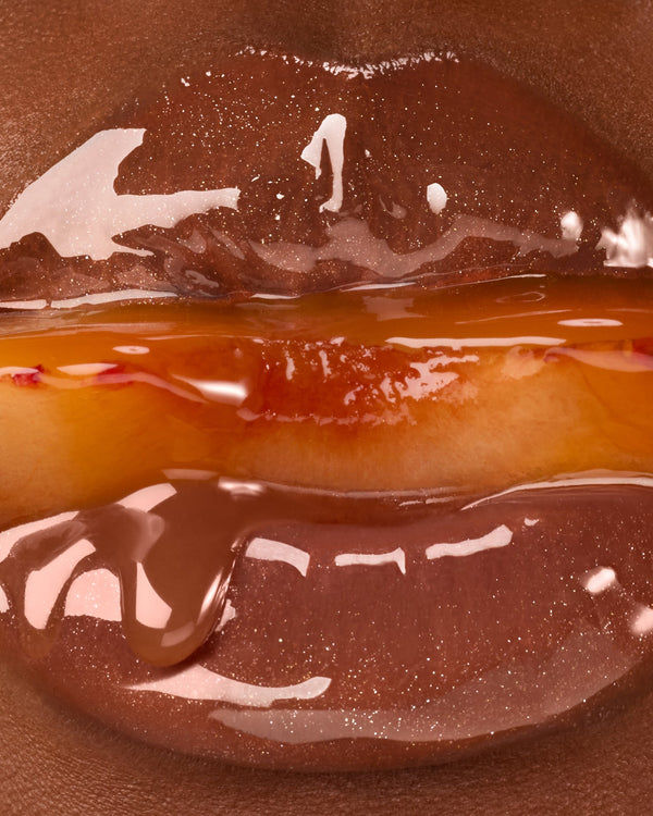 Close up of glossy lips holding a plum.