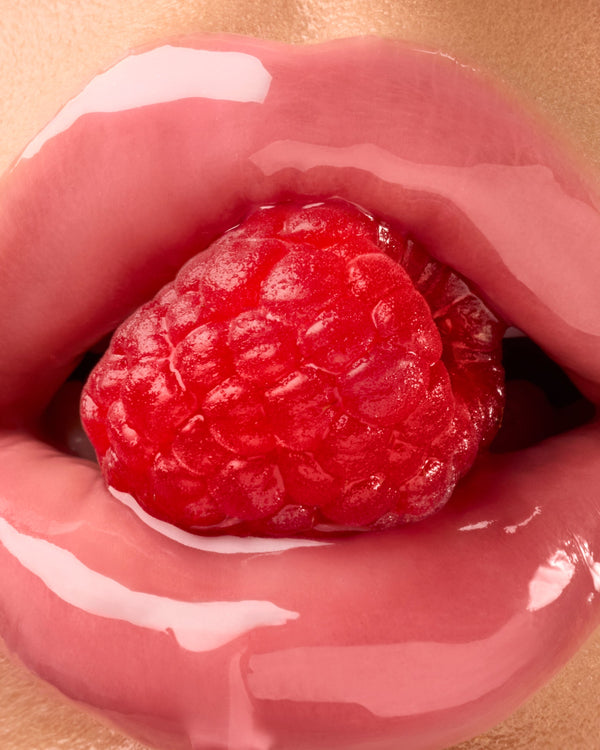 Glossy lips surrounding a raspberry.