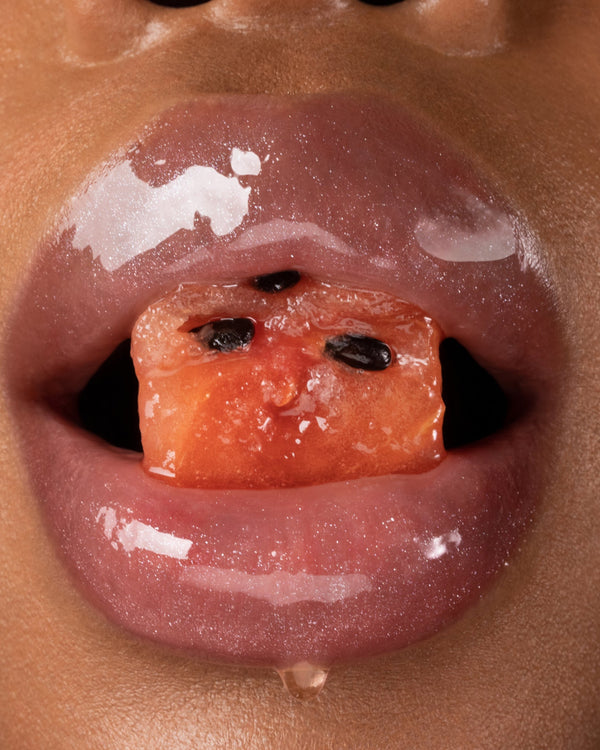 Glossy lips holding a piece of watermelon.