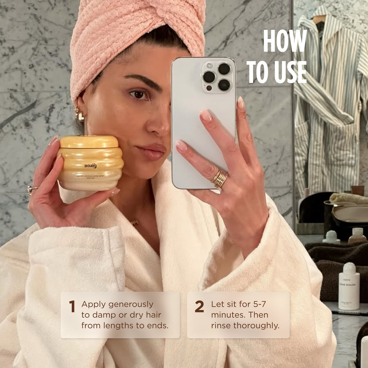 Model in a pink towel turban and robe holding the Gisou Honey Gloss Ceramide Therapy Hair Mask, with application steps: apply to damp or dry hair, then rinse after 5-7 minutes.