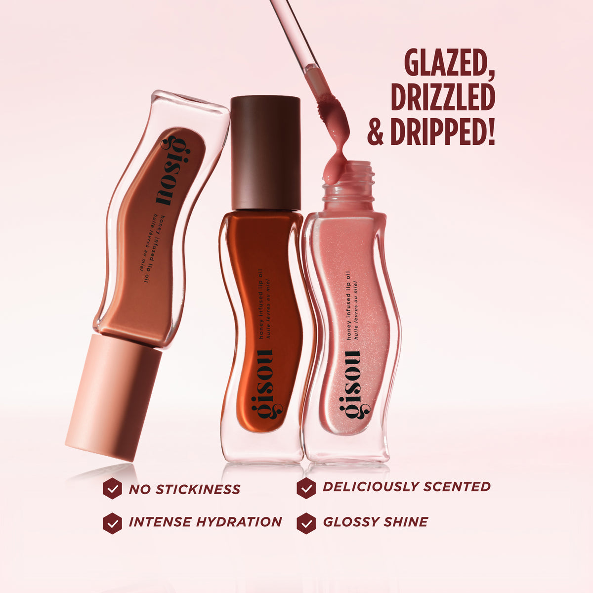 Three Gisou Honey Infused Lip Oil Fall Collection bottles in different shades, one with its wand out, listing benefits: intense hydration, glossy shine, no stickiness, and deliciously scented.