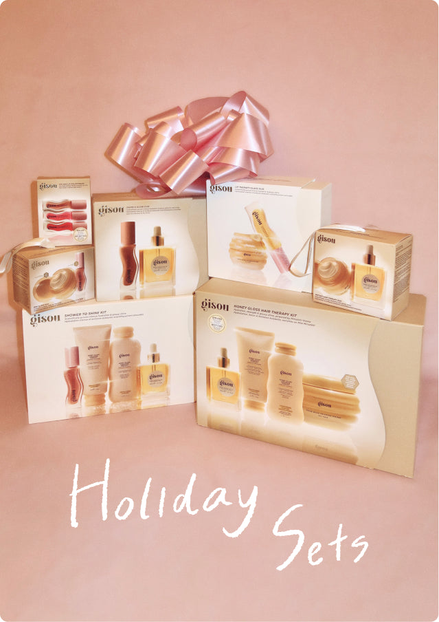 Stack of Gisou holiday gift sets with a large pink ribbon bow on a pink background
