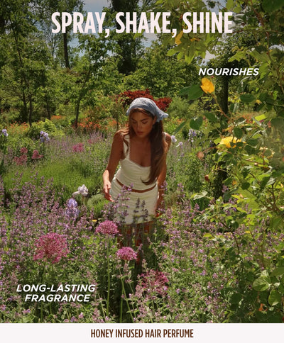 Model in a headscarf and white dress walking through a wildflower garden, promoting the Gisou Honey Infused Hair Perfume for its nourishing, long-lasting fragrance.