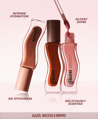 Three Gisou Honey Infused Lip Oil Fall Collection bottles in different shades, one with its wand out, listing benefits: intense hydration, glossy shine, no stickiness, and deliciously scented.