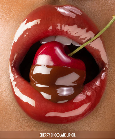 Close-up of glossy lips biting into a cherry stem, promoting the Gisou Cherry Chocolate Lip Oil.