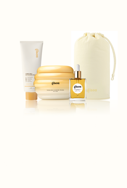 Gisou Honey Milk 5-in-1 Styling Cream, Honey Gloss Ceramide Therapy Hair Mask, Honey Infused Hair Oil, and a Gisou Honey Glow Hair Towel pouch grouped together on white.