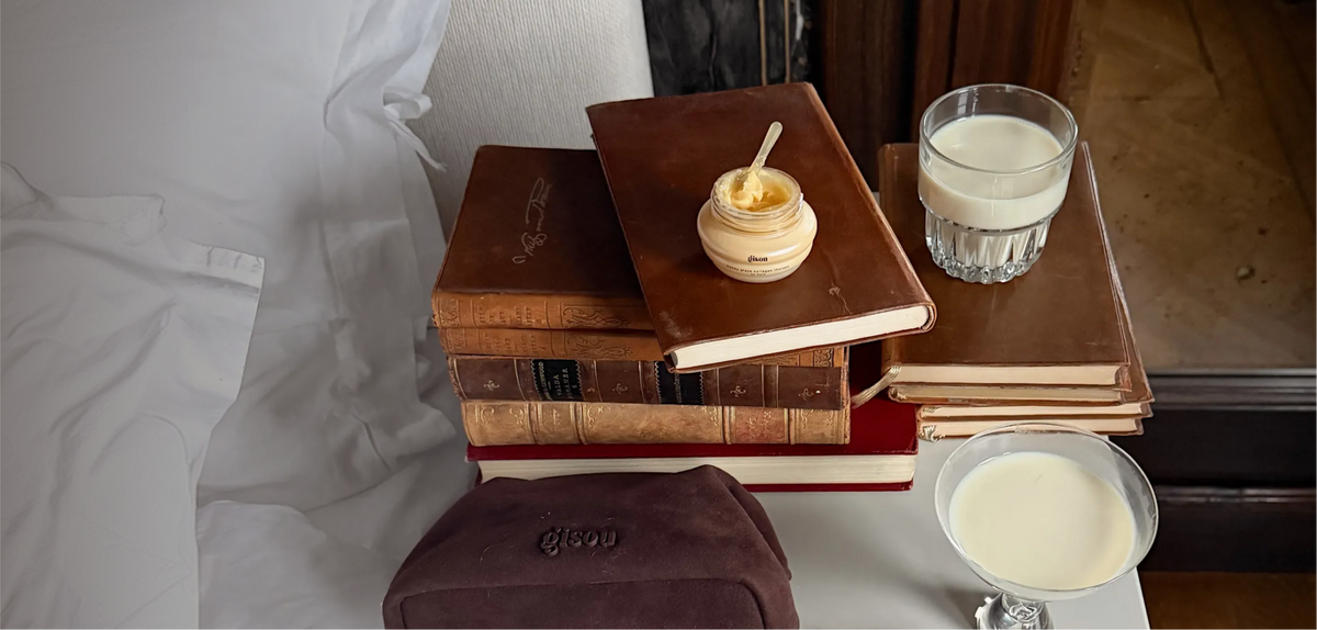 A shot of Gisou Honey Hair Mask placed onto an old book next to Gisou Choco Suede Pouch.