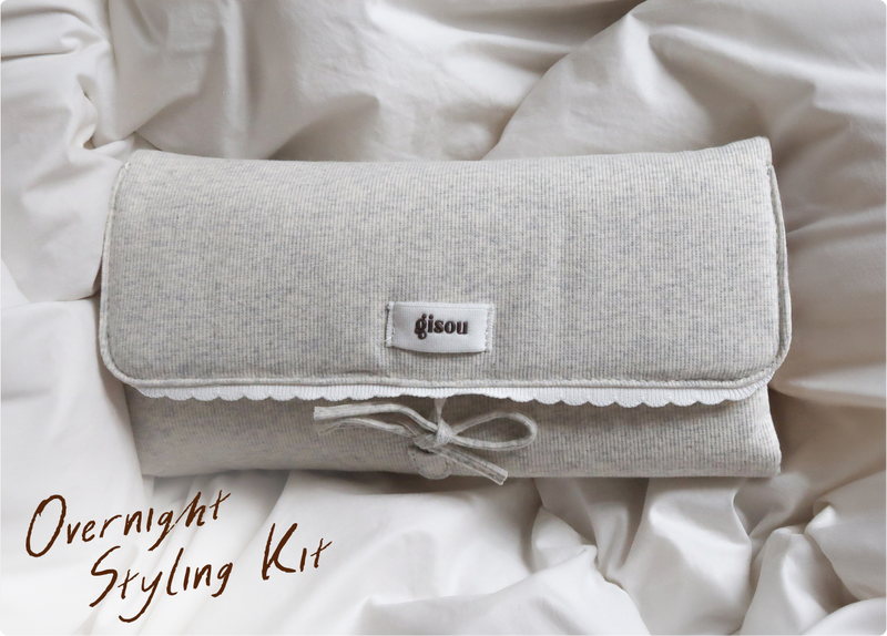The Gisou Overnight Styling Kit pouch laying on the bedsheets.