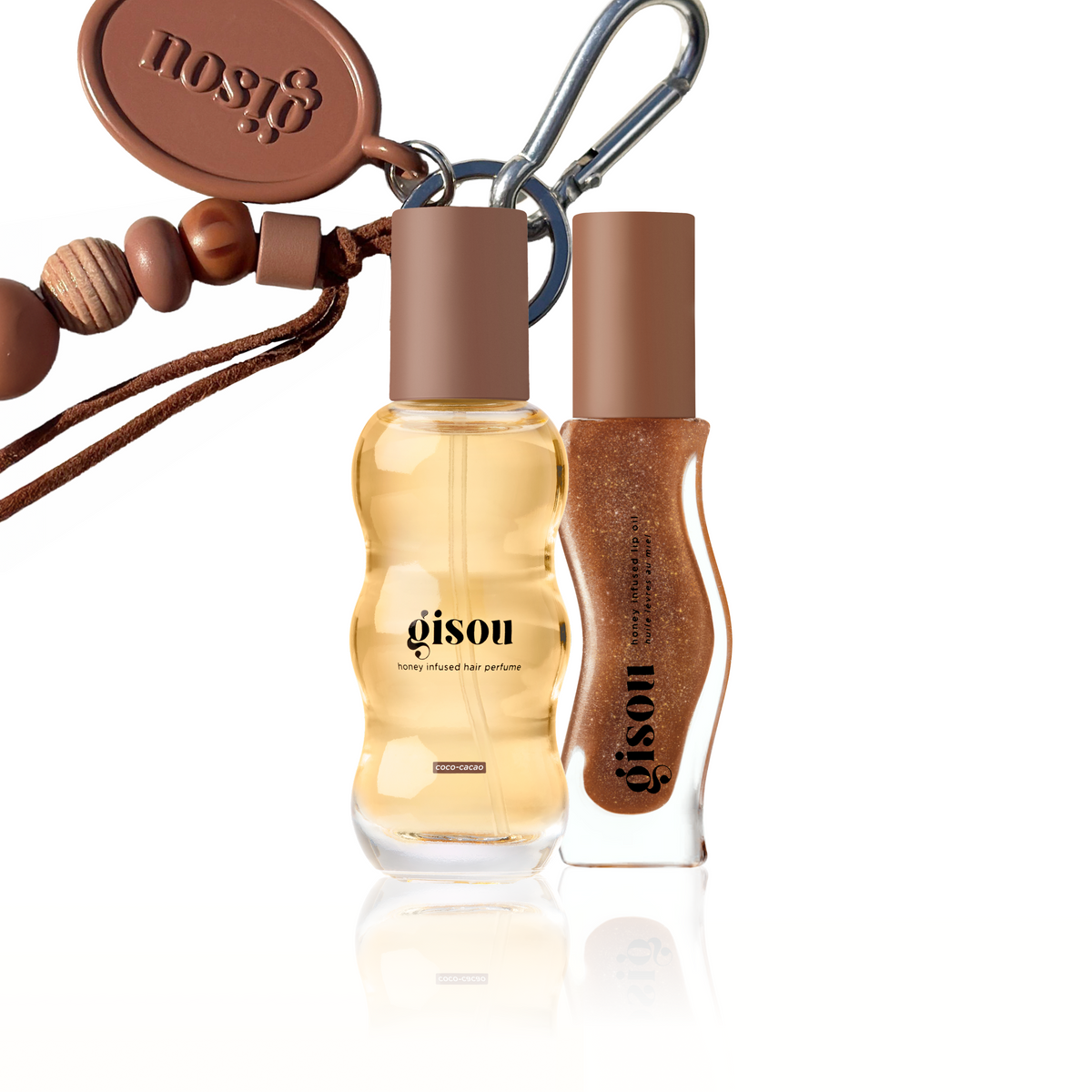 Bundle featuring the Honey Infused Hair Perfume Limited Edition Coco-Cacao Gourmand Edition, the Honey Infused Lip Oil Limited Edition Coco-Cacao, and an exclusive beaded keychain charm. The hair perfume appears in a warm caramel-gold tone, while the lip oil has a rich cocoa-brown shimmer with fine golden sparkle, creating a cosy chocolate-inspired colour palette with glossy finishes and metallic silver hardware.