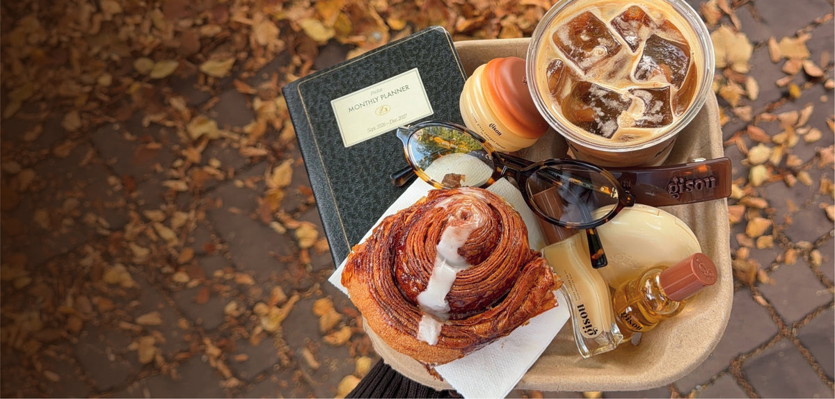 Gisou products on a tray with iced coffee and a cinnamon bun among autumn leaves