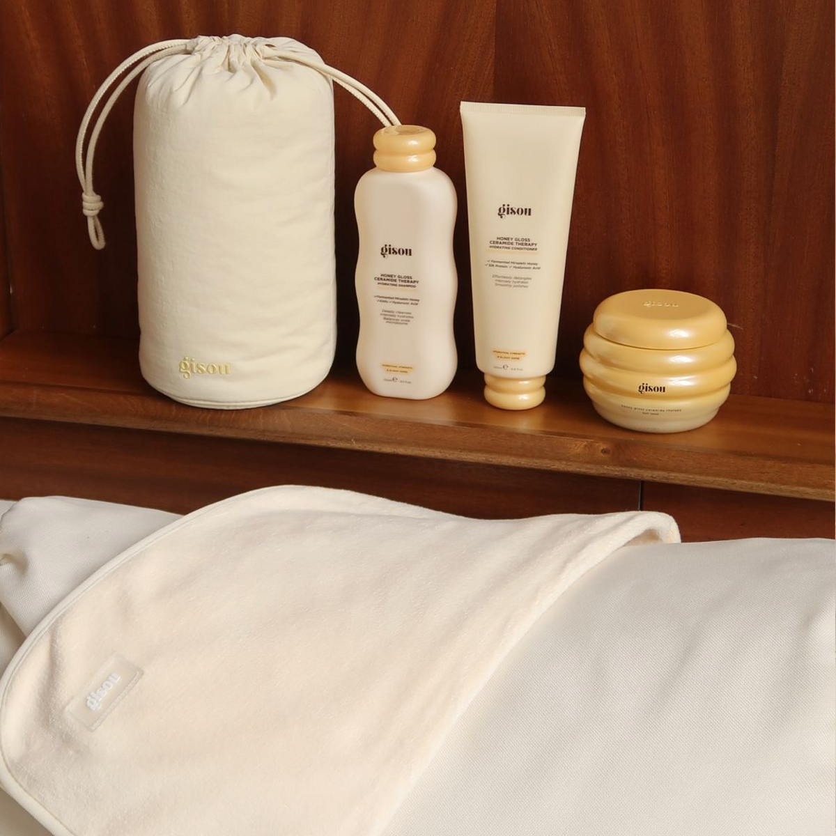Gisou Honey Gloss Microfiber Hair Towel next to Shampoo, Conditioner and Hair Mask on a wooden background.