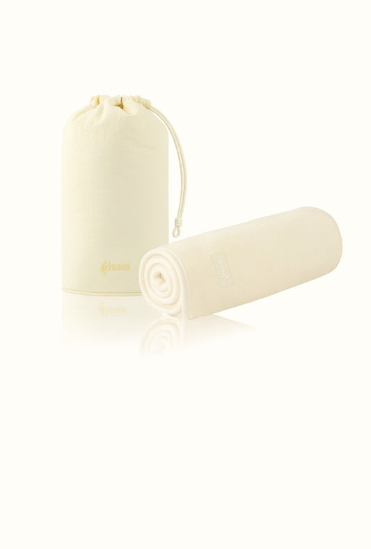 Two Gisou Honey Gloss Microfiber Hair Towels, one folded upright in a pouch and one rolled, on white.