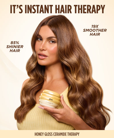 Model with long wavy brunette hair holding the Gisou Honey Gloss Ceramide Therapy Hair Mask, listing 85% shinier and 19x smoother hair.
