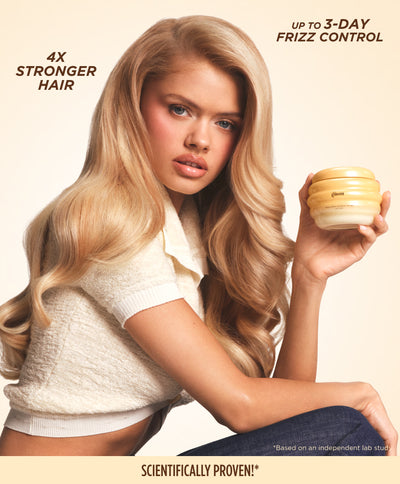 Model with long wavy blonde hair holding the Gisou Honey Gloss Ceramide Therapy Hair Mask, listing 4x stronger hair and up to 3-day frizz control.