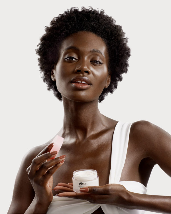 A dark-skin model holding a jar of Honey Infused Hair Mask Travel Size