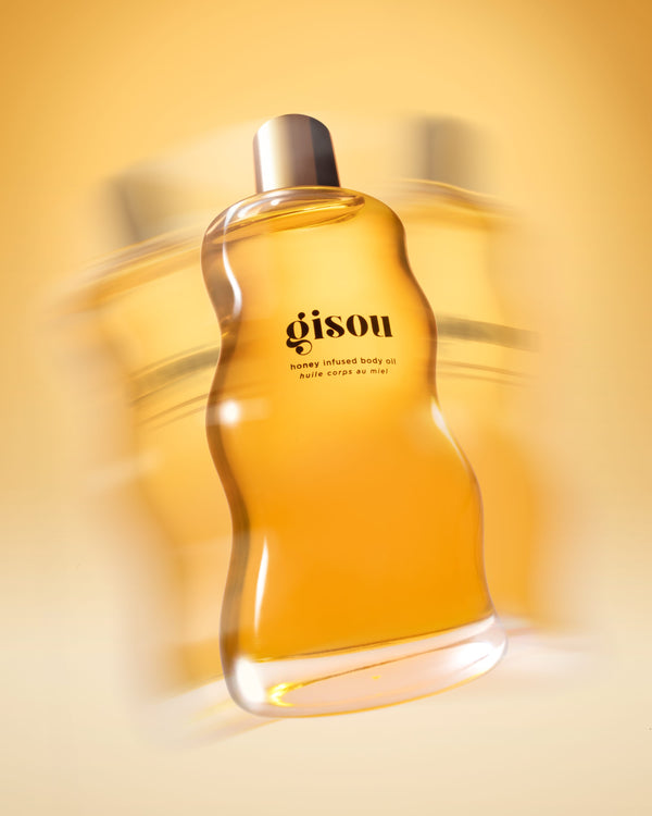 A bottle of the honey infused body oil shaking on the yellow background