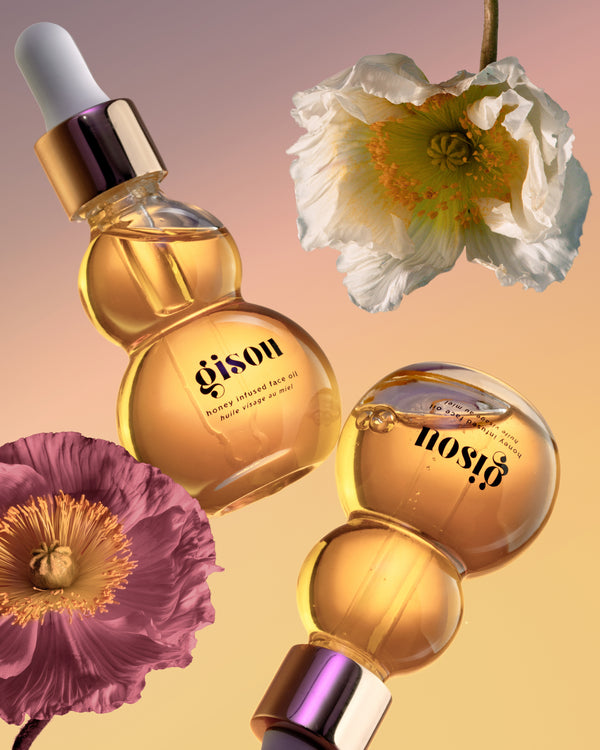 Bottles of the Honey Infused Face Oil suspended on air with flowers around